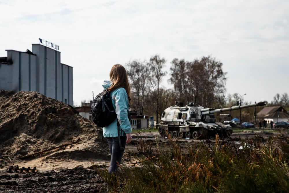 Child stands in front of ruined city and a military tank