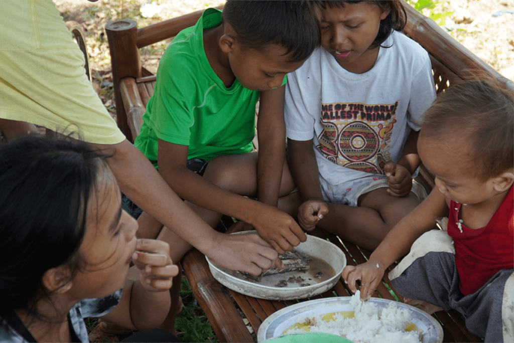 A family, including small children, are sharing very little fish and rice for lunch