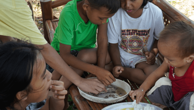 A family, including small children, are sharing very little fish and rice for lunch